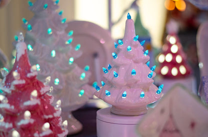 A close-up of a small white Christmas tree night light with glowing blue lights, surrounded by other decorative holiday lights in soft focus.