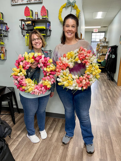 Two women holding flower wreaths in a store setting